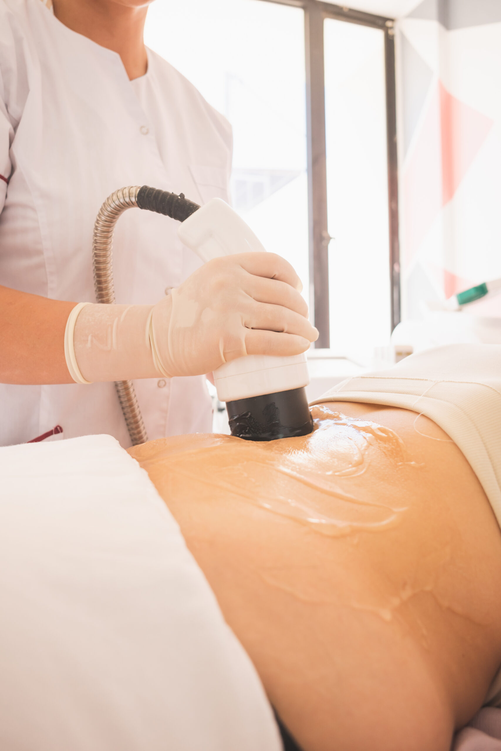 Vertical shot of female physical therapist doing ultrasonic cavitation therapy on a woman in spa
